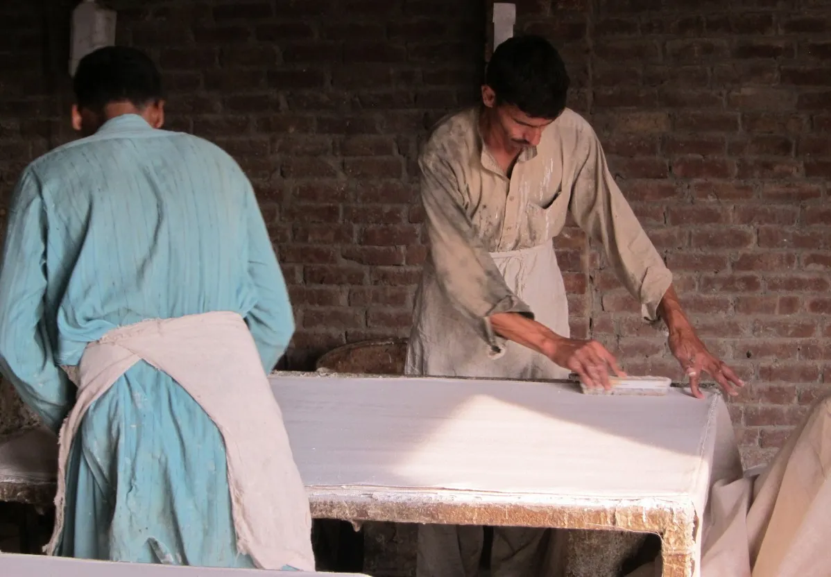The rexine lamination process; workers are gluing layers of cotton and polyester fabric onto the sheets of artificial leather (rexine) from which the exterior of the ball will be formed.
